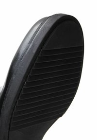 Semelle de chaussure noire au design plat, avec une texture striée pour une meilleure adhérence. Bord lisse avec une légère courbure au talon.