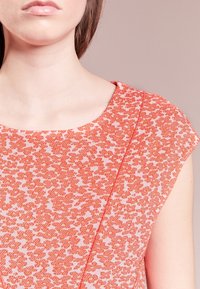 Blusa con estampado de coral que presenta un escote redondo, mangas cortas y tela texturizada con un diseño sutil sobre un fondo claro.