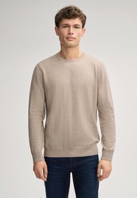 Hellbeige langärmliger Pullover mit rundem Halsausschnitt und gerippten Bündchen, kombiniert mit dunklen Jeans. Weiche Textur und schlichtes Design.
