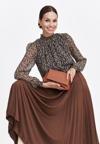 Czarna bluzka w kwiaty z bufkami, brązowa plisowana spódnica i torebka w kolorze rdzy. Widoczne są gładkie tekstury i kontrastujące wzory.