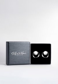 Orecchini d'argento con accenti di perle esposti in una scatola regalo nera testurizzata con testo del logo in argento. La scatola è aperta e mostra gli orecchini all'interno.