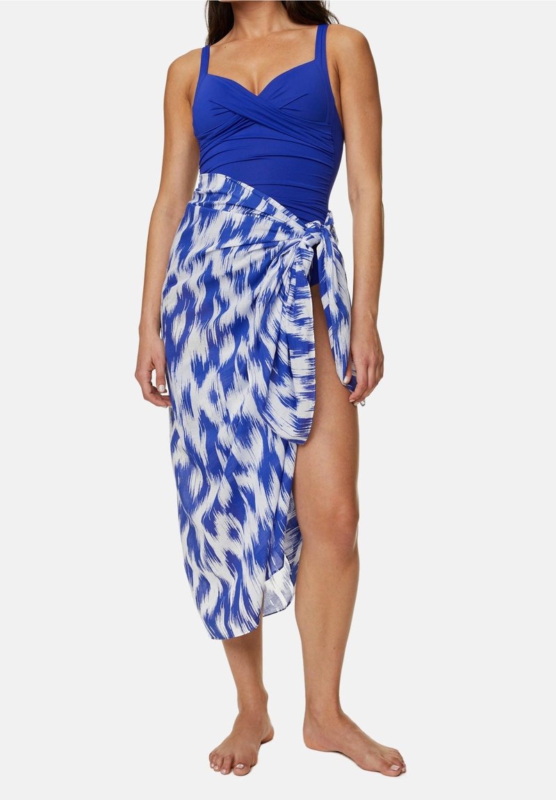 Femme portant un maillot de bain une pièce bleu avec un sarong blanc et bleu à motifs noué à la taille, laissant une jambe découverte.