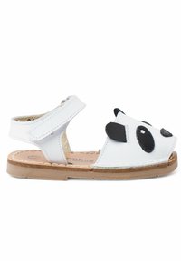 Sandales en cuir blanc avec un design de visage de panda noir, à lanière ajustable, orteils ouverts, semelle texturée brune et doublure intérieure rembourrée.