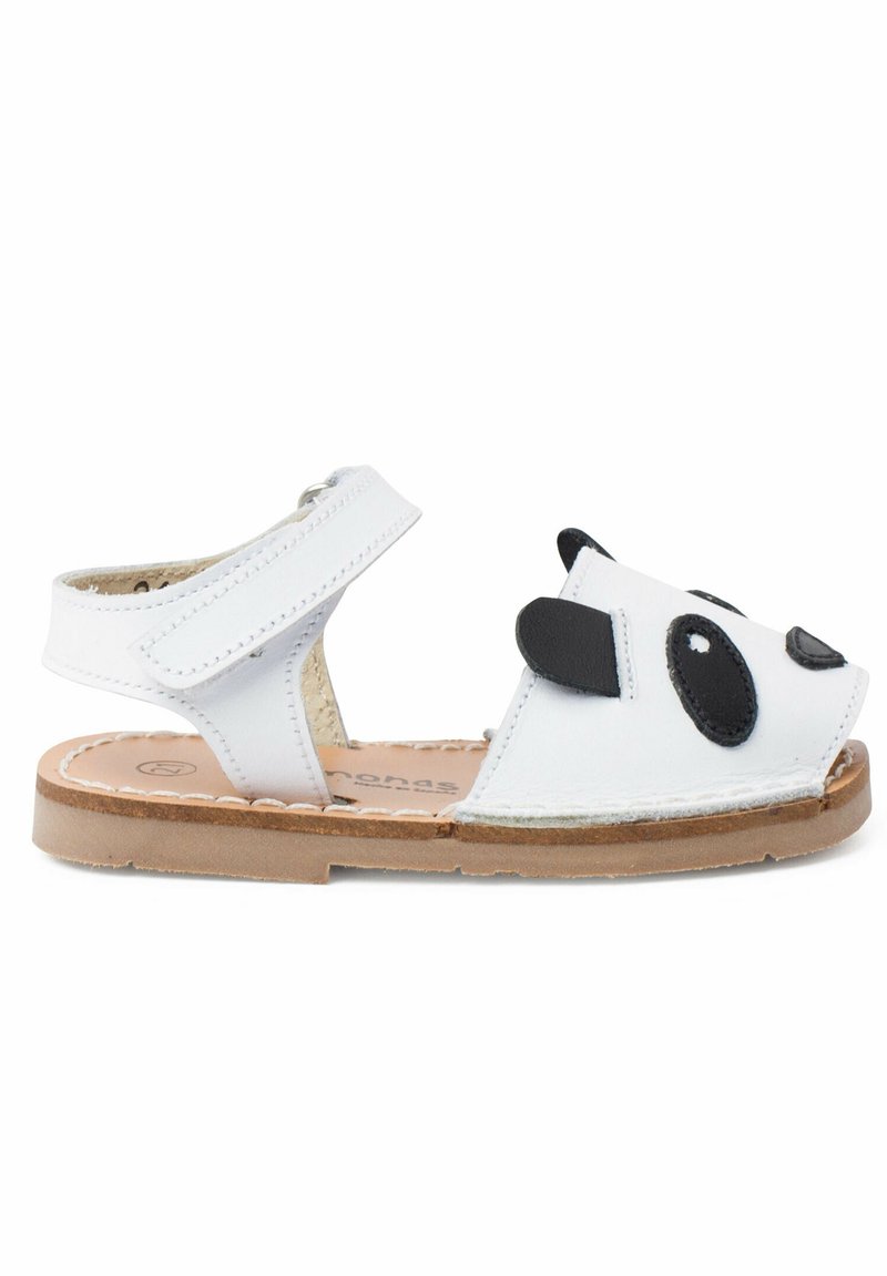 Sandales en cuir blanc avec un design de visage de panda noir, à lanière ajustable, orteils ouverts, semelle texturée brune et doublure intérieure rembourrée.