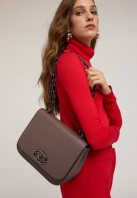 Bolso de cuero marrón con un diseño elegante, con una correa de cadena negra y un cierre con un logo destacado. Textura suave con acentos mínimos.