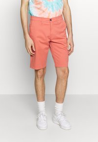 Pantaloni corti corallo realizzati in tessuto misto cotone, con taglio dritto, tasche frontali e chiusura con bottone. Abbinati a sneaker bianche e calzini.