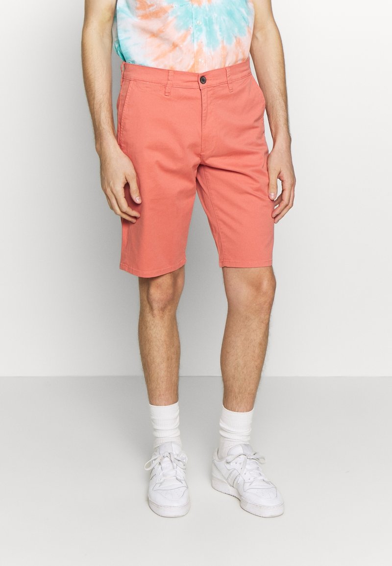 Pantaloni corti corallo realizzati in tessuto misto cotone, con taglio dritto, tasche frontali e chiusura con bottone. Abbinati a sneaker bianche e calzini.