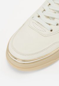 Baskets en cuir blanc avec un bout rond, des lacets plats et une semelle intermédiaire rehaussée d'or. La surface est lisse avec des détails cousus.