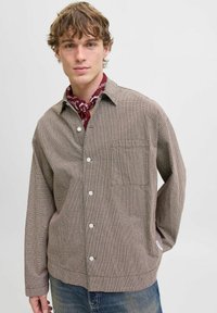 Brown checkered button-up shirt with a chest pocket. Features a relaxed fit and long sleeves, layered over a red bandana.