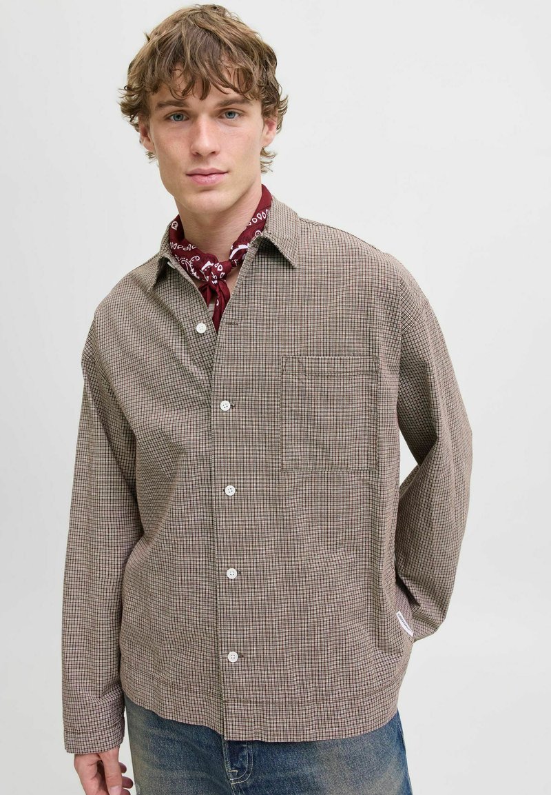 Brown checkered button-up shirt with a chest pocket. Features a relaxed fit and long sleeves, layered over a red bandana.