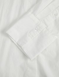 Camisa de algodón blanca con puños abotonados, que presenta una textura suave y un diseño minimalista, resaltando los detalles de costura y los botones.