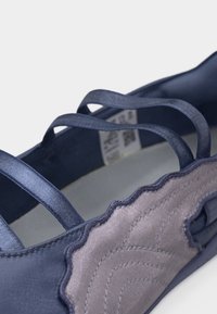 Κοντινή λήψη ενός ναυτικού μπλε παπουτσιού με πολλαπλές ελαστικές λουράκια και λεπτομέρεια ραμμένης, υφής με κυματοειδή άκρη.