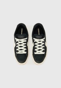 Black sneakers with white laces, featuring a suede and leather upper, perforated toe detail, and rubber outsole with subtle red accents.