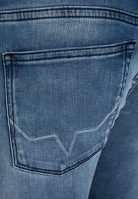 Jeans de mezclilla en un lavado azul claro, con un bolsillo trasero que presenta un distintivo detalle de costura en punta y una textura ligeramente desgastada.
