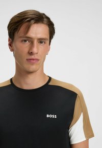 Czarny T-shirt z rękawami w kolorze beżowym, białym i kremowym, podzielonym na bloki kolorystyczne. Posiada okrągły dekolt i białe logo 'BOSS' na klatce piersiowej. Gładka tekstura.
