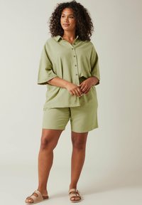 Vaaleanvihreä puuvillainen lyhythihainen paita ja siihen sopivat shortsit. Napillinen etuosa, rento malli, tekstuuriaines, jota täydentävät beige sandaalit.