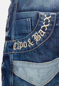Jeans in denim con un lavaggio blu scuro, caratterizzati dal logo ricamato "Cipo & Baxx", una tasca posteriore e un accento in tessuto blu più chiaro.