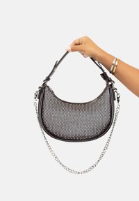 Bolso de cuero negro con remaches metálicos, forma redondeada, una correa de cuero corta y una cadena desmontable para opciones de transporte versátiles.
