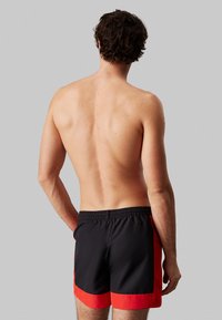 Pantaloni da bagno neri con dettagli rossi, cintura elastica e un design elegante. Il tessuto sembra morbido e leggero, ideale per le attività acquatiche.