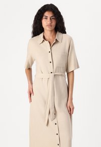 Abito a camicia in tessuto beige chiaro con una texture morbida, maniche corte, tasca a pattina e una cintura coordinata in vita.