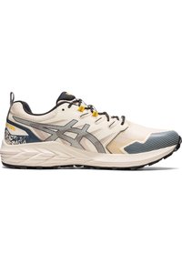 Chaussure de course beige et noire avec semelle à motif, lacets noirs, œillets jaunes et marquage gris foncé sur le côté.