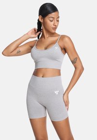 Sivina športna modrc in kratke hlače, izdelane iz mehkega in raztegljivega materiala. Opremljene so z belimi logotipskimi poudarki in prilegajočim se dizajnom za aktivno nošenje.