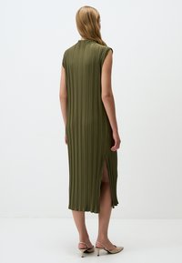 Olivgrünes, plissiertes Kleid mit hohem Kragen und seitlichen Schlitzen, aus einem strukturierten Stoff gefertigt. Ärmelloses Design und fließende Silhouette.