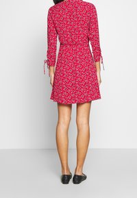 Rotes Blumenkleid mit langen Ärmeln und Bindetails, mit einem taillierten Bund und ausgestelltem Rock, aus leichtem Stoff gefertigt.
