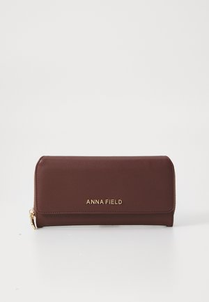 Cartera de cuero sintético marrón con logotipo de marca dorado, cierre de cremallera y un diseño delgado y rectangular. Textura suave con acentos mínimos.