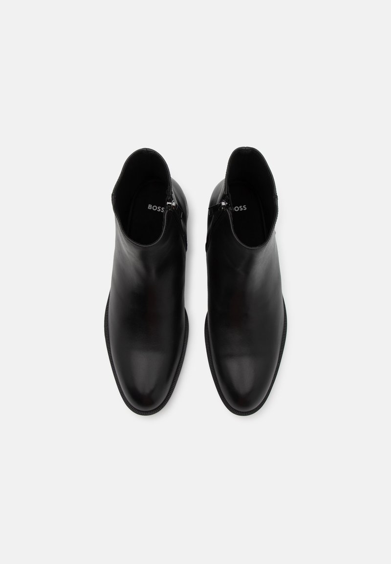 Bottines en cuir noir avec une finition lisse, bout en amande et zip sur le côté. L'intérieur affiche l'étiquette de la marque "BOSS" en blanc.