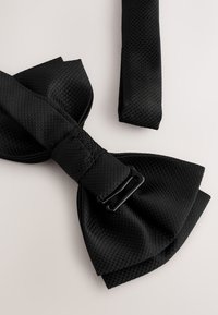 Black mesh bow tie with a textured surface; features a woven strap and a black clip for fastening. The design is classic and formal.
