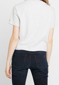 Grå bomulls t-shirt med korta ärmar, cropped design. Kombinerad med mörkblå denimjeans med bakfickor och subtila sömmar.