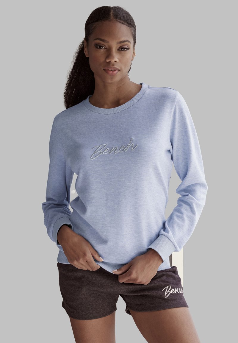Sudadera azul clara con el logo de "Bench" bordado y pantalones cortos oscuros marrones a juego con un diseño similar. Material de algodón, corte casual.