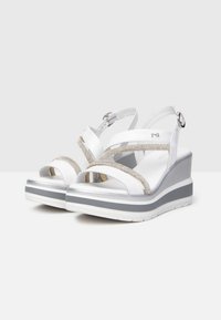 Sandalias de cuña blancas con una parte superior texturizada, acentos metálicos y una suela de plataforma en capas en gris y blanco. Incluye una correa ajustable en el tobillo.
