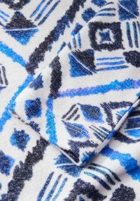 Barevný textil s geometrickým vzorem v modré, černé a bílé. Měkká textura s různými tvary a akcenty po celém povrchu.