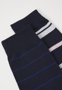 Gestreifte Socken aus dunkelblauem Stoff mit geripptem Bund. Eine Socke hat dünne blaue Streifen, die andere hat breitere Pastellstreifen.