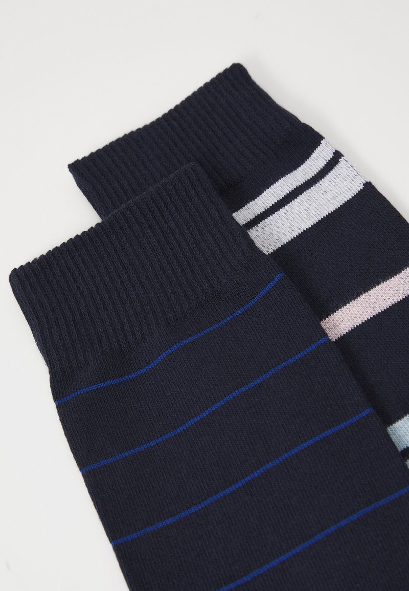 Chaussettes rayées en tissu bleu marine foncé avec des bords côtelés. Une chaussette présente de fines rayures bleues, tandis que l'autre a des rayures pastel plus larges.