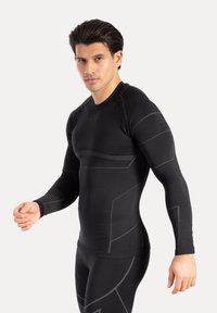 Czarna, dopasowana koszulka kompresyjna z długim rękawem, wykonana z fakturowanej tkaniny, z szarymi geometrycznymi akcentami na rękawach i torsie.