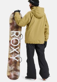 Rumena nepremočljiva jakna, črne snežne hlače in črne rokavice. Snežna deska s potiskom gozdnih motivov in belim logotipom "ROXY".