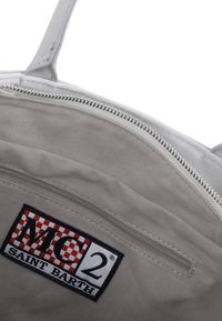 Intérieur d'un sac en tissu gris avec une poche zippée. Il comporte une étiquette de marque "MC2 SAINT BARTH" avec un motif damier rouge et noir.