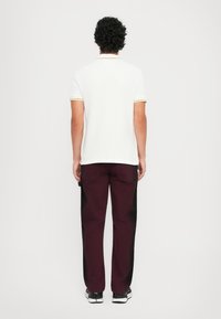 Hvit polo-skjorte med gule stripete mansjetter, kombinert med mørk burgunder bukser. Antrekket har en avslappet passform og uformelt design.