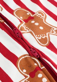 Piros és fehér csíkos textil, amelyen mézeskalács sütik mintázata látható, a közepén egy piros cipzárral. Puha tapintású.