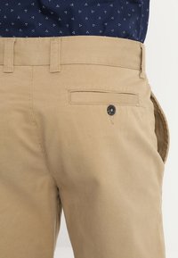 Pantaloni corti in cotone beige con una tasca posteriore con chiusura a bottone, tessuto strutturato e vita aderente.