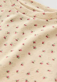 Tissu beige avec de petits motifs floraux roses. Texturé avec de petits trous, featuring un col côtelé pour plus de détail.