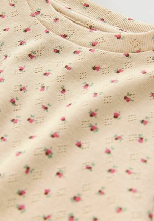 Tissu beige avec de petits motifs floraux roses. Texturé avec de petits trous, featuring un col côtelé pour plus de détail.