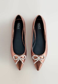 Puntige ballerina's in metallic rosegoud fake leer. Voorzien van een gemetalliseerde strikaccent op de tepunt. Zwarte binnenvoering en een gladde textuur.