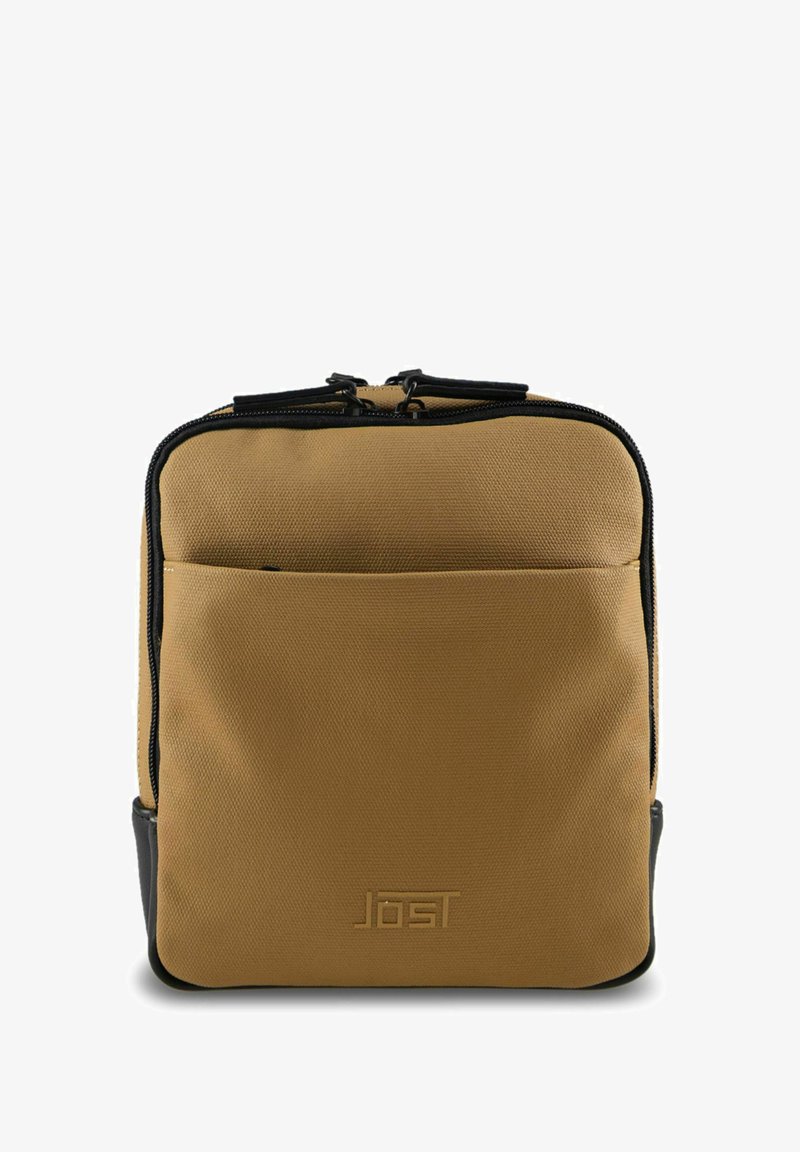 Sac à dos en tissu beige avec accents noirs, fermeture éclair, poche avant et logo embossé sur le bas avant, présentant une surface texturée.