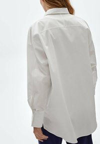 Chemise blanche à manches longues avec boutons et col pointu, confectionnée dans un tissu lisse, dotée d'une coupe décontractée et d'un ourlet légèrement arrondi.