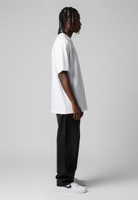 Bílý oversized tričko s krátkým rukávem, spárované s černými volnými džínami a bílými teniskami s černým akcentem.