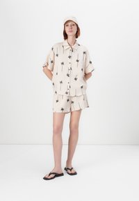 Kremfarget skjorte med krage og matchende shorts med svart palme mønster. Brukt med svarte flip-flops og en lys farget caps.